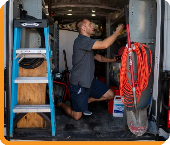 Technician in a Pro-Tec uniform adjusting settings on a gray HVAC unit.