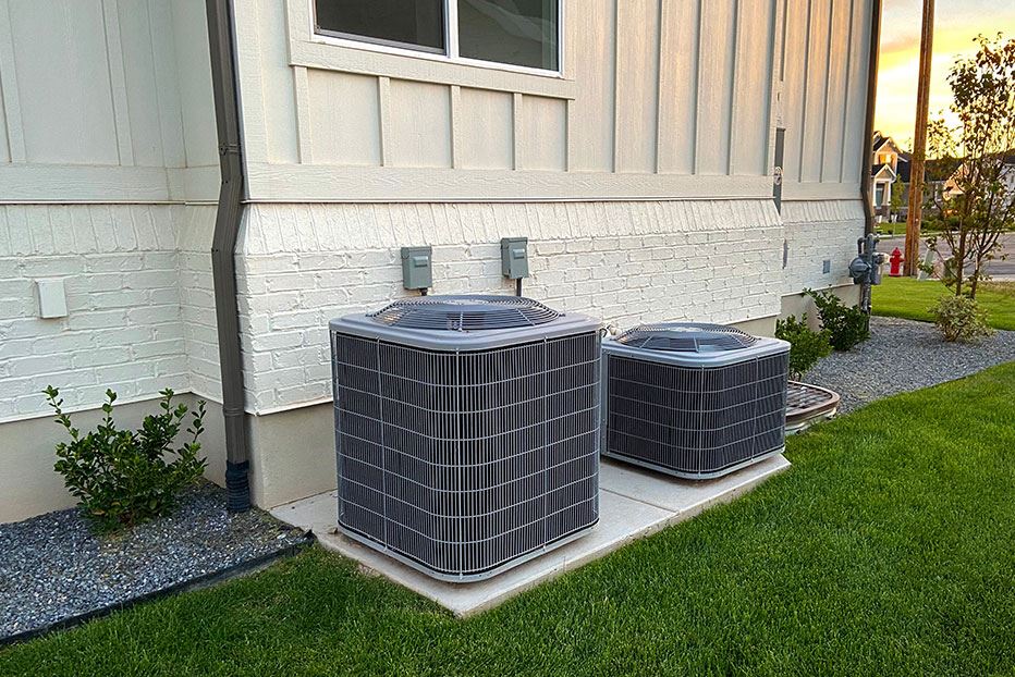 Double AC units outside white brick home with green landscape and gravel