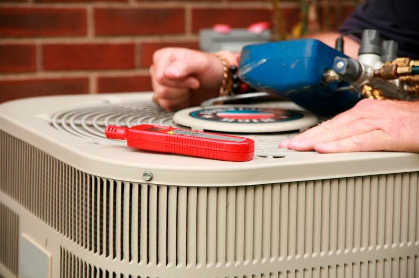 Angled view of a technician's hands and tools rested on an AC condenser unit